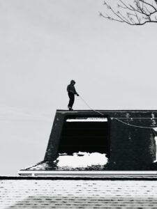 A homeowner uses a soft roof rake from the ground to remove leaves from asphalt shingles.